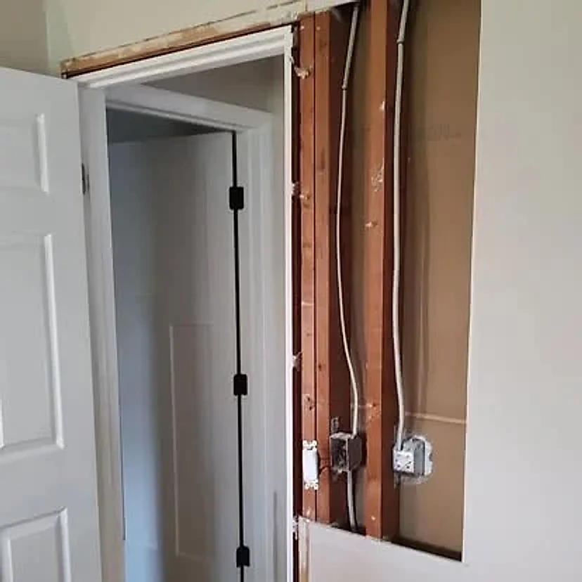 Wall beside a doorway opened to expose the framing and wiring