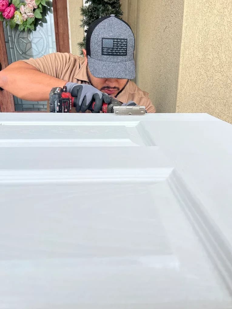 Technician using a power tool to fit a hinge to a white paneled door