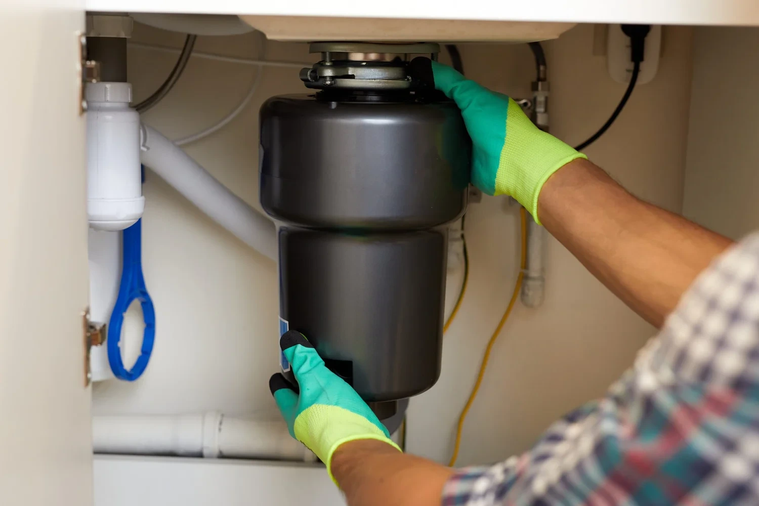 Gloved hands fitting a garbage disposal unit under a sink
