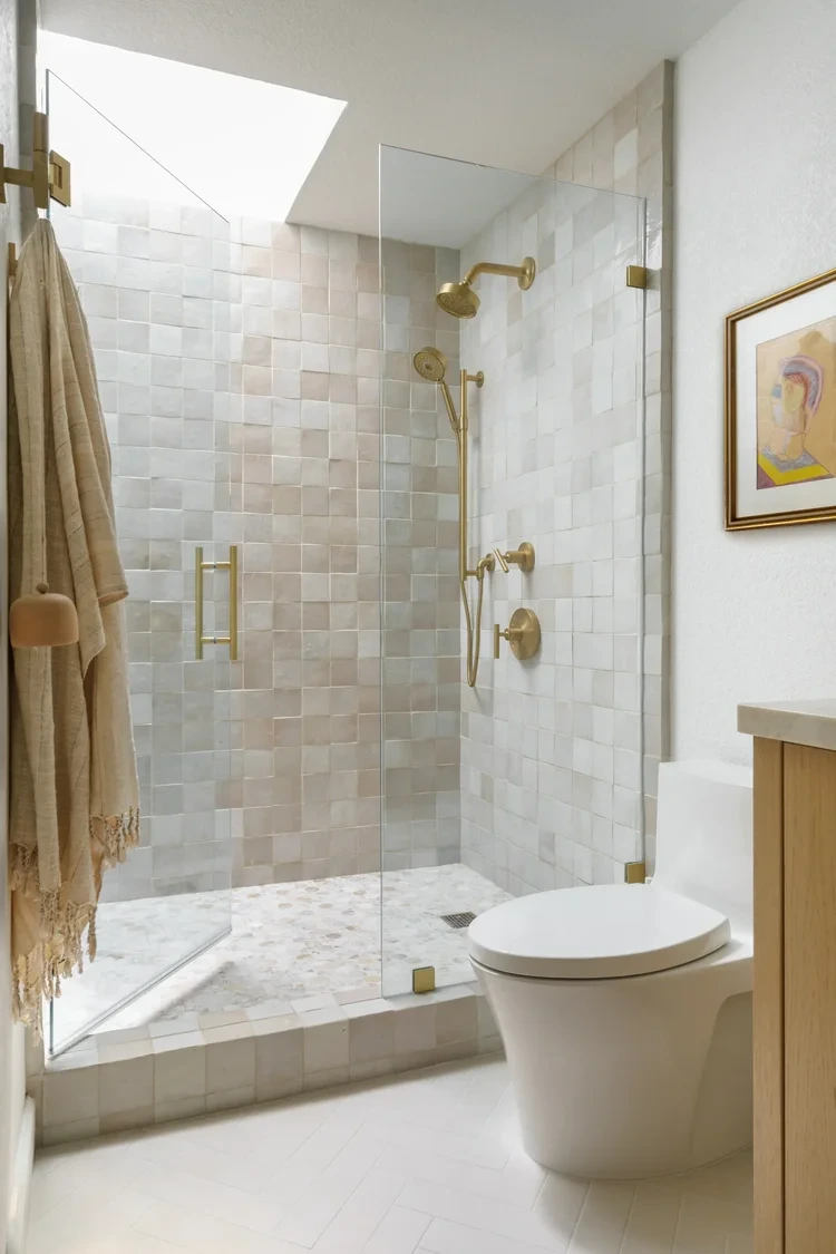 Tiled shower enclosure with brushed brass fixtures and glass door
